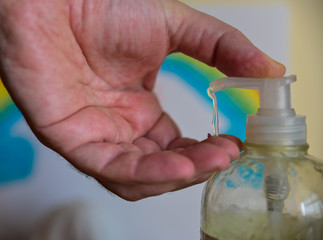 How to kill viruses and bacteria. Close up shot on bottle spout with selective focus. Caucasian man's hand  dispenses gel. Blurred background with rainbow design.
