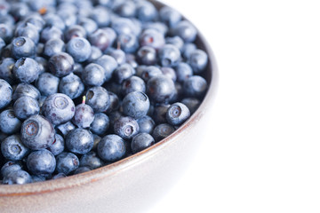 Fresh bilberry in a bowl on a white surface, close-up
