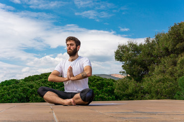 Naklejka na ściany i meble Young man on a terrace in summer, doing yoga exercise. Meditation Namaste pose.