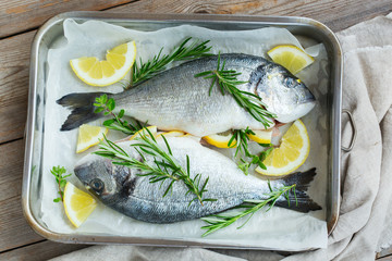 Fresh raw dorado fish with lemon, rosemary on kitchen table