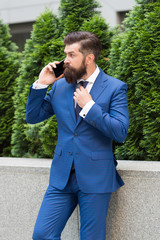 handsome mature entrepreneur using phone. confident man standing outdoors at the city street. communication. mature bearded man near cypress tree. successful businessman outdoors