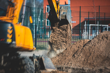 Yellow heavy excavator excavating sand and working during road works, unloading sand during construction of the new road with workers around