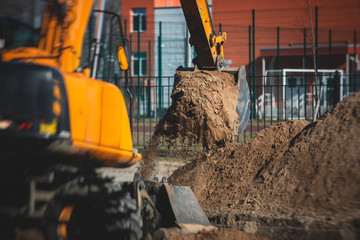 Fototapeta premium Yellow heavy excavator excavating sand and working during road works, unloading sand during construction of the new road with workers around