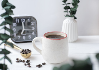 Breakfast relax time concept. coffee mug on a cozy kitchen table with alarm clock and green plants in vase. scandinavian minimal style. coffee beans in a spoon. time for yourself to start a good day.