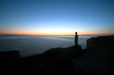 silhouette of man looks at a beautiful seascape at sunset