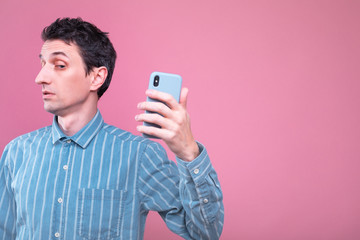 Young man stand on left side and take picture or selfie. Guy in blue shirt posing on camera alone. Isolated over pink background.