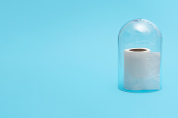 Half roll of toilet paper in quarantine under a glass cloche dome on a blue background with copy space and room for text with a right side composition.