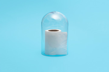 Half roll of toilet paper in quarantine under a glass cloche dome on a blue background with copy space and room for text