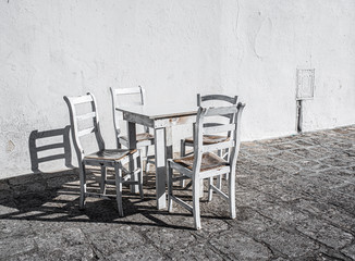 White empty dining wooden table and chairs  in a street cafe. White concrete wall in the background.