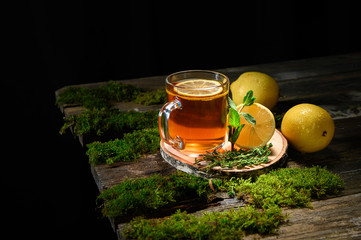 glass mug with fresh black tea with lemon and mint on an old wooden table