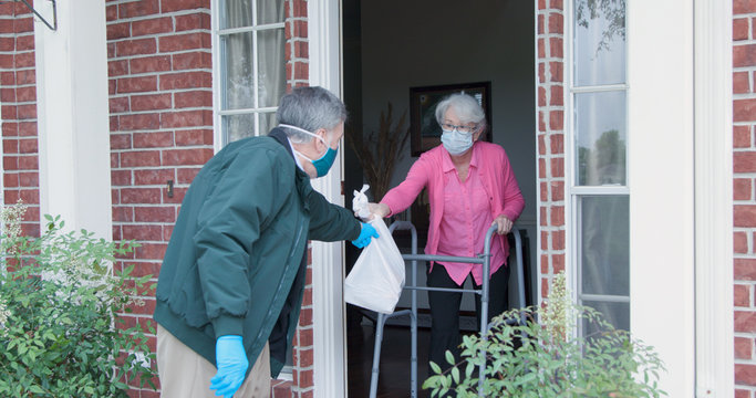 An elderly woman with a walker who is at high risk because of the coronavirus COVID19 gets meals or groceries delivered to her house by a volunteer working with a benevolent organization.