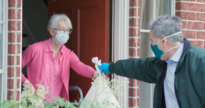 An Elderly Woman Using A Walker Receives Meals From A Man Working With A Benevolent Group Delivering Food To Those Who Are At High Risk Because Of The Coronavirus COVID19.