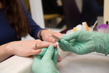 Woman hands in a nail salon receiving a manicure. Nail filing. Close up, gloved master