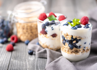 White yogurt in glass jar with raspberries and blueberries on grey napkin.