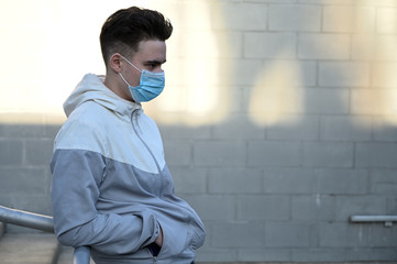 Portrait of a Caucasian young man in a medical mask outdoors in the city on a gray background on a...