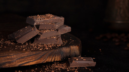 Banner with bitter chocolate on a wooden Board. Chocolate and coffee on a dark background. Chocolate chip. Low key. Copy space. Horizontal orientation. Shooting concept for cafes and restaurants
