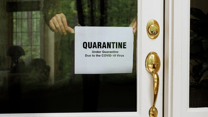 Coronavirus pandemic notice. Man hangs Covid-19 virus self quarantine sign in window of house front door. Home entry door quarantine warning announcement.