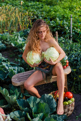 Attractive brunette harvesting vegetables: tomatoes, cucumbers, cabbage, peas, eggplants, peppers
