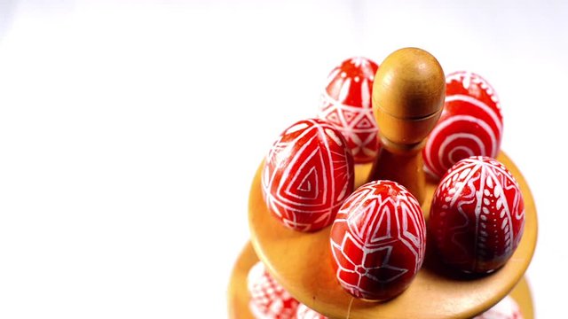 Red easter eggs with folk Ukrainian pattern lay and revolve on wooden stand for eggs which stand in right side on white background. Ukrainian traditional eggs pisanka and krashanka.
