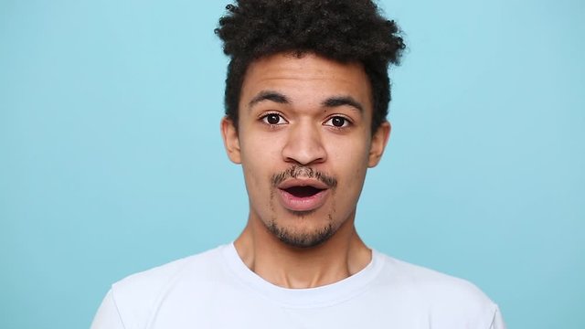 Unshaven shocked surprised african american young guy 20s in white t-shirt isolated on pastel blue background studio portrait. People sincere emotions lifestyle concept. Look at camera wow open eyed