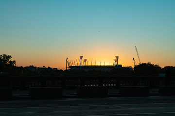 Melbourne Cricket Ground stadium silhouetted by bright rising morning sun.