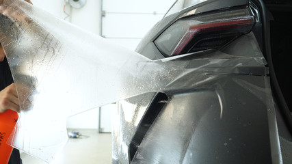 Close up of paint protection film installation on modern luxury car. PPF is polyurethane film that wrap car paint to protect paint surface from stone chips, bug splatter, and abrasion.