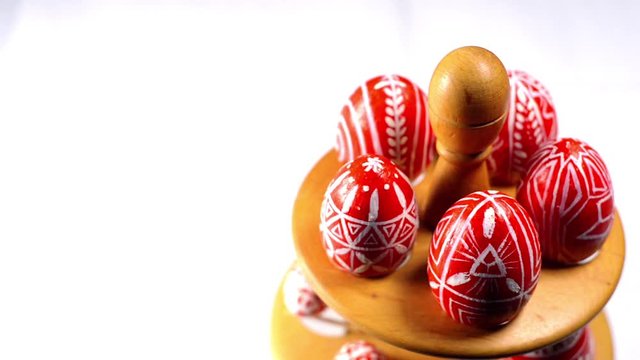Red easter eggs with folk Ukrainian pattern lay on wooden stand for eggs. And man rotate one egg on white background. Ukrainian traditional eggs pisanka and krashanka.