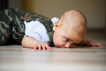 little boy aged 8 months in overalls, a white shirt and white socks crawling on the floor and...