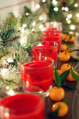 Candles in glass candlesticks stand on a shelf with a luminous garland and tangerines.
