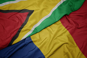 waving colorful flag of romania and national flag of guyana.