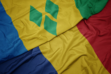 waving colorful flag of romania and national flag of saint vincent and the grenadines.