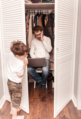 Busy father trying to find a quiet place in a wardrobe  to hide from children for a work at the...