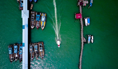 Fototapeta na wymiar Aerial view of a boat passing by other boats in an asian styled harbour with fishing boats. Green waters, old boats, two lines with boats. 