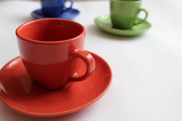 red Cup and saucer on a white background green and blue cups and saucers in the background