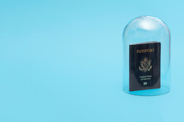 US passport in quarantine under a glass cloche dome on a blue background with copy space and room for text with a right side composition