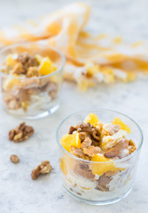 Dessert laid out in layers from pieces of cookies, fruits and cream, decorated with nuts in glass glasses on a light background, vertical arrangement