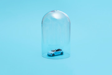 Blue convertible car in quarantine under a glass cloche dome on a blue background with copy space and room for text 