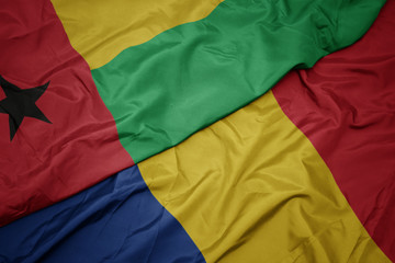 waving colorful flag of romania and national flag of guinea bissau.