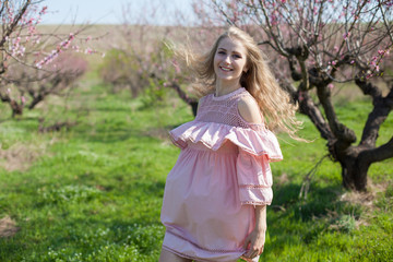 Fototapeta na wymiar Beautiful blonde woman in pink dress in flowering peach garden in spring