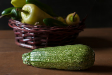 Fresh Zucchini on a wooden table with chiles ina a basket in the background, dark food photography, low key light.