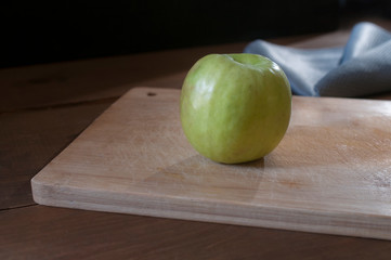 Green apple on an old cutting board with a blue napkin and rim light at the background, rustic...