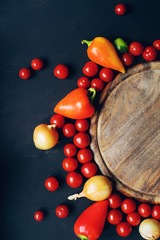 Mix of colorful raw fresh cherry tomatoes, pepper and onion  on dark stone table and empty old wooden board