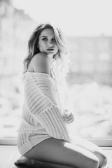 Beautiful pregnant woman in a white transparent blouse on the background of a window in the backlight. Black and white photo. Fine art. Expectation of a child. Soft selective focus.