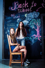 back to school after summer vacations, two teen real girls in classroom with blackboard painted together, lifestyle people concept