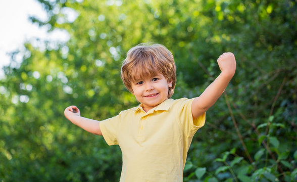 Child outdoors in nature. Happy child. Funny baby boy isolated on a background of green trees. Smiling child boy. Cheerful cheerful kid. Happy children kid boy with hands up