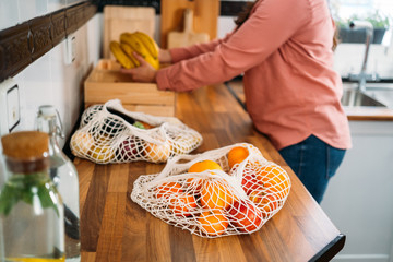 Woman keeping the purchase of fruit in her kitchen. Using a reusable organic cotton mesh bag on...