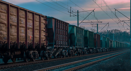 Fototapeta premium Railway at the end of a warm day. The train carries wagons with goods. Sunset at the station.