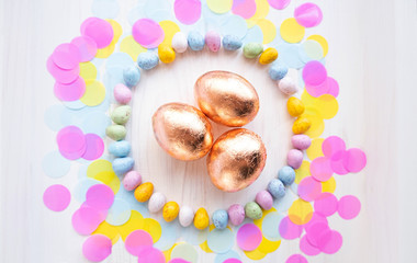 Easter golden eggs on colorful confetti background. Circle frame made of colorful small eggs. Flatlay. Easter party 