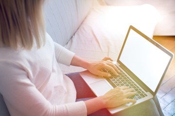 Fototapeta premium Portrait of blonde hair woman using her blank screen laptop while sitting on the sofa at home in the sunset light. Blonde female sit indoors at home working on computer with blank screen. Home office 