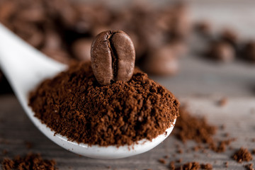  white ceramic spoon with ground coffee on a wooden background Fried Arabica grains